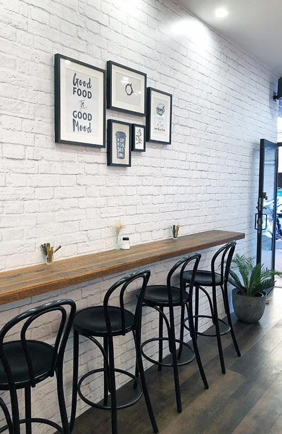 Timber bench with black bentwood stools along a white brick wall with framed prints, inside Monty's Sandwich Shop
