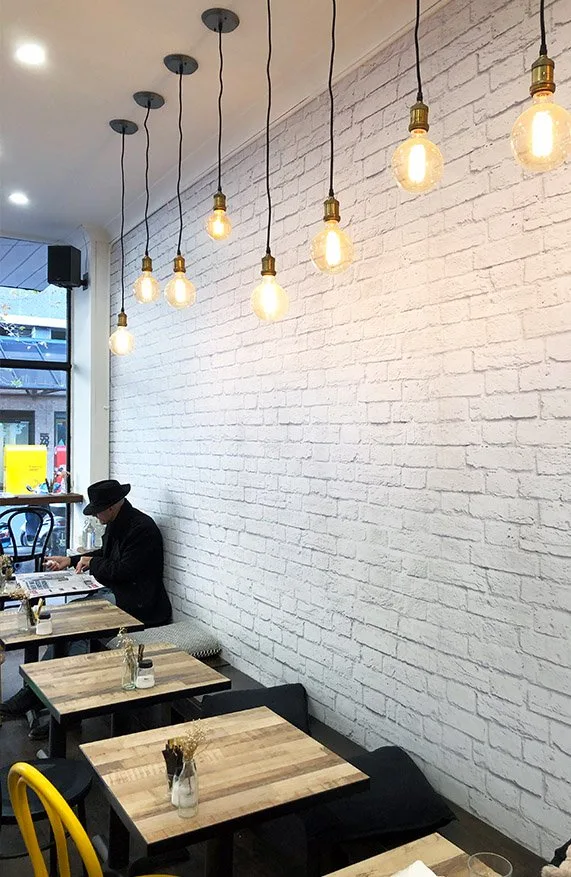 Inside Monty's Sandwich Shop, with timber tables, pendant lights and a white brick wall by the front window