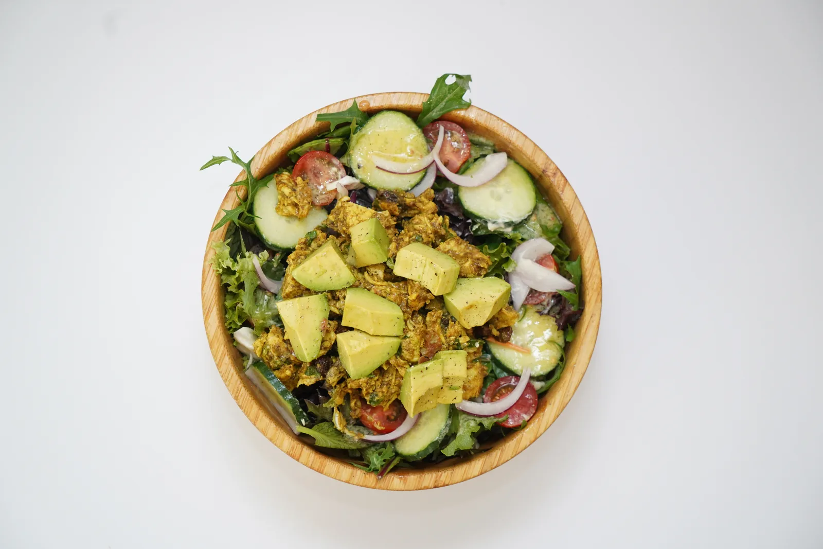 Coronation Chicken & Avocado Salad in a wooden bowl, with mixed leaves, cucumber, cherry tomatoes and red onion