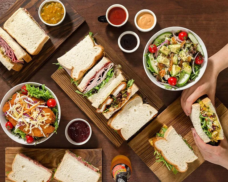 Sandwiches cut in halves on wooden boards with salads and sauces, from Monty's Sandwich Shop in Bondi Junction